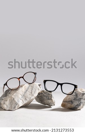 Two pairs of trendy glasses in plastic frame on stones on light background. Glasses sale poster. Optic store sale-out offer. Copy space for text. For banner, web line. Optic store discount Royalty-Free Stock Photo #2131273553