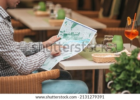 Young man searching for place of destination. Caucasian tourist looking at the map of European city in outdoor cafe