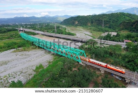 Aerial view of a Chu-Kuang express train traveling on a truss iron bridge across a dry riverbed with beautiful mountains in background on a sunny summer day, in Ruisui Township, Hualien County, Taiwan Royalty-Free Stock Photo #2131280607