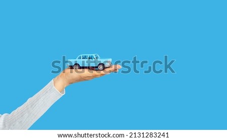 Little car on open woman's hand on blue text copyspace studio background, cropped shot. Salesperson or driver holding little auto. Adult person playing with toy car. Insurance, rent, lending concept Royalty-Free Stock Photo #2131283241