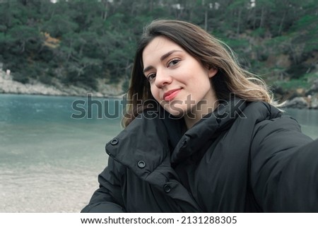 Beautiful girl taking selfie in front of beautiful sea and mountain view. She is so happy and smiling. 