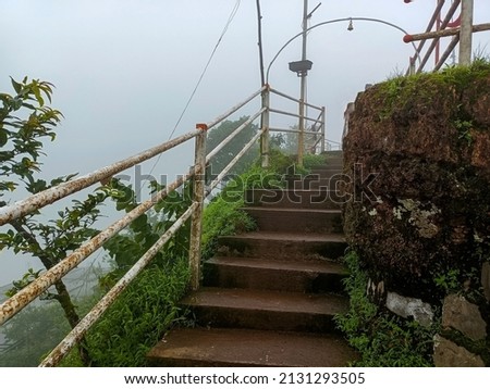 Stock photo of ancient staircase made by stone in the old hindu temple sateri Mahadev mandir, there is white color iron stairs railing and small bell . Picture captured during rainy season.