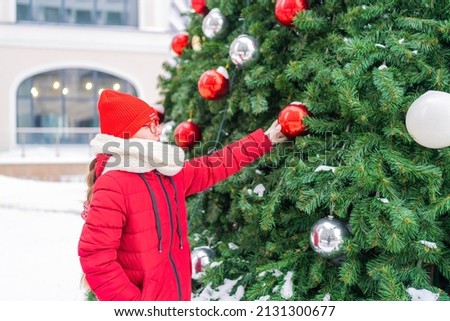 girl in red jacket and hat standing near a large Christmas tree