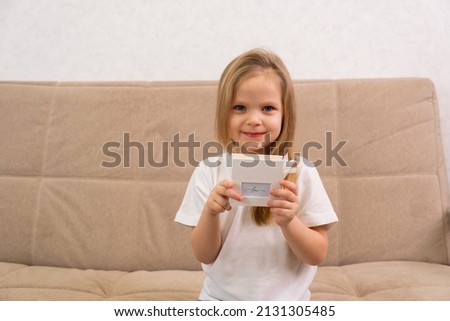 beautiful young blonde girl is sitting on the couch, looking at the camera and holding a gift box in her hands