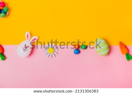 Top view festive Easter pink and yellow background with colored eggs, decorative carrots, bunny rabbits, flowers, chocolate eggs. Creative bright Easter. Flat lay. Copy space.