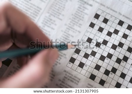 Close up hand holding pencil over crossword puzzle on newspaper. Game on for writing some letters to solve and completing the empty table. Royalty-Free Stock Photo #2131307905