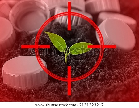 a small green sprout against the background of plastic waste, lids in the focus of the red sight.