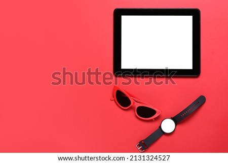 Tablet computer, smart watch and sunglasses on red background
