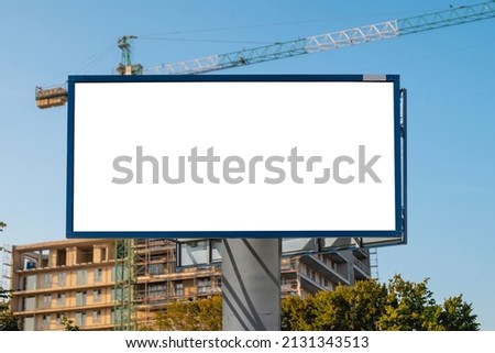 Blank white billboard for advertisement in front of the construction site. There is modern apartment building in the background.