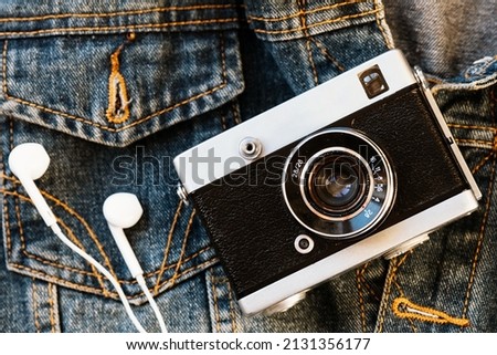 Film camera and white wired headphones lie against background of denim. Fashionable hipster background. Retro style. Photographer's Day. Top view