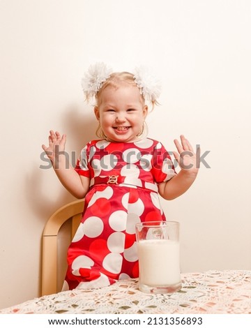 a cheerful two-year-old girl in a red polka dot dress and a large mug of milk