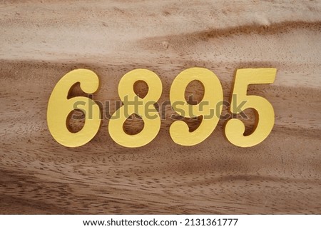 Wooden  numerals 6895 painted in gold on a dark brown and white patterned plank background.