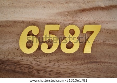 Wooden  numerals 6587 painted in gold on a dark brown and white patterned plank background.