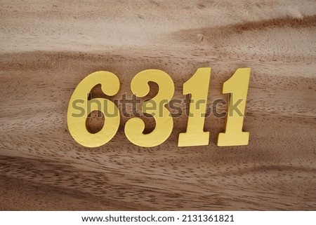 Wooden  numerals 6311 painted in gold on a dark brown and white patterned plank background.