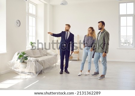 Real estate agent giving potential buyers or future tenants tour about big new house. Boyfriend and girlfriend or husband and wife who plan property investment looking at lovely modern spacious home Royalty-Free Stock Photo #2131362289