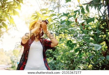 The low-level angle of young beautiful Asian traveling woman wears hat taking photos of beautiful landscape in the forest while on vacation at the forest. Adventure travel photo camera concept holiday