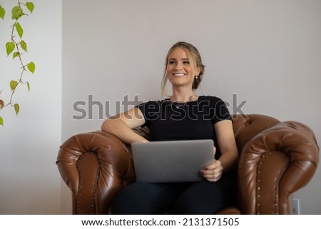Young woman working at home with laptop on a brown arm chair with a white background. Home office concept. Gray notebook for working. Home office concept. High quality photo