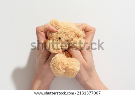 Hand holding squashed teddy bear toy isolated on white background. Concept of a friend and love. A mother holds a small brown toy bear on a palm isolated.	