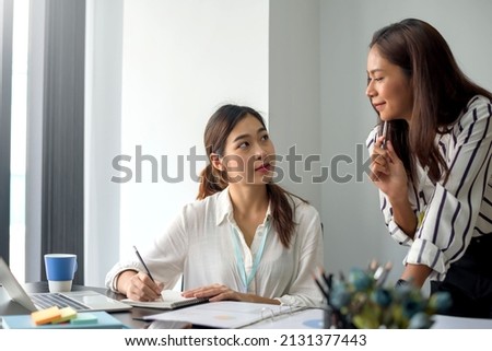 Two Smiling young Asian businesswoman talking to colleague, employees brainstorming, sitting working at office