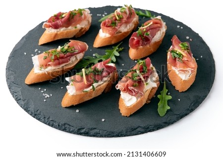 Platter of delicious crostini topped with cheese, rocket salad and prosciutto crudo, italian appetizers Royalty-Free Stock Photo #2131406609
