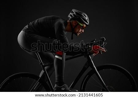 male cyclist riding road bicycle on black background Royalty-Free Stock Photo #2131441605