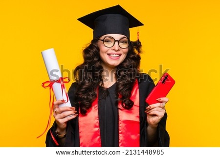 Girl graduate in graduation hat and eyewear with diploma and smartphone on yellow background. Online broadcast of presentation of certificates of education and speech of best student. Royalty-Free Stock Photo #2131448985