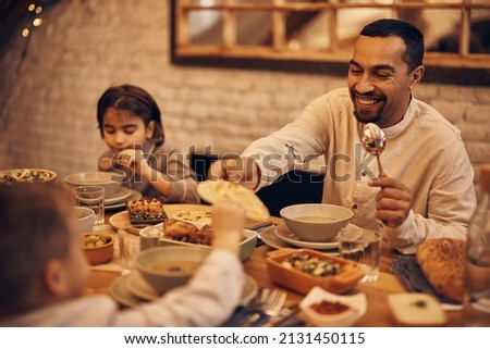 Happy Muslim father and son sharing pita bread during family meal at dining table during Ramadan.  Royalty-Free Stock Photo #2131450115