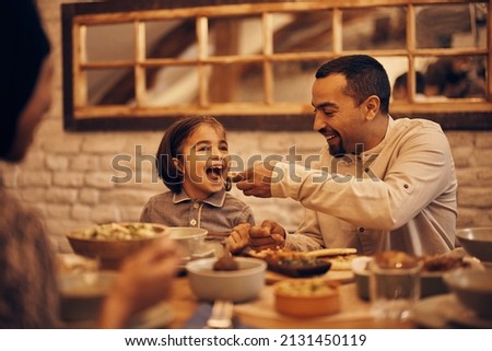 Happy Muslim little girl having fun while father is feeding her while having dinner at home on Ramadan.  Royalty-Free Stock Photo #2131450119