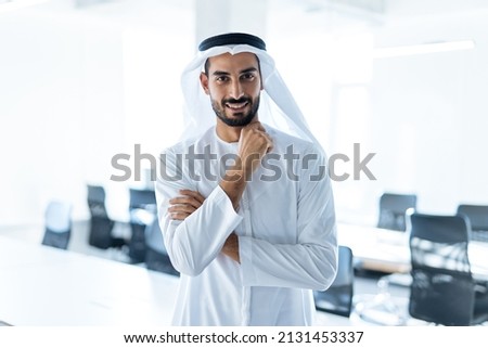 handsome man with dish dasha working in his business office of Dubai. Portraits of a successful businessman in traditional emirates white dress. Concept about middle eastern cultures Royalty-Free Stock Photo #2131453337