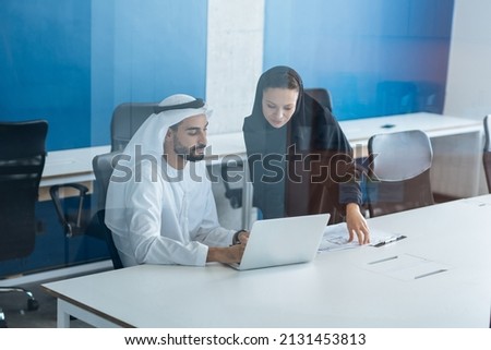 Man and woman with traditional clothes working in a business office of Dubai. Portraits of  successful entrepreneurs businessman and businesswoman in formal emirates outfits. Concept about middle east Royalty-Free Stock Photo #2131453813