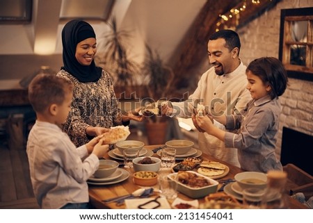 Happy Muslim parents and their kids sharing pita bread while eating dinner on Ramadan at home.  Royalty-Free Stock Photo #2131454041
