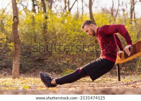 Active man doing bodyweight dips while working out outdoors in street workout park on a sunny autumn day Royalty-Free Stock Photo #2131474125
