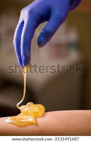 Woman's hand in a medical glove holds yellow sugar paste or wax for depilation close up