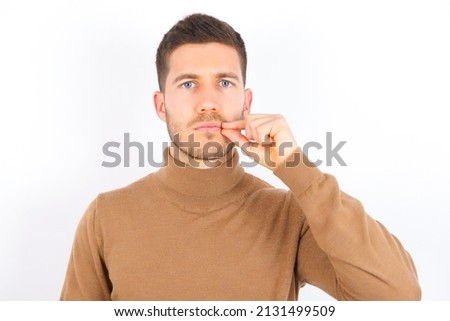 young caucasian man wearing turtleneck over white background mouth and lips shut with fingers. Secret and silent, taboo talking.