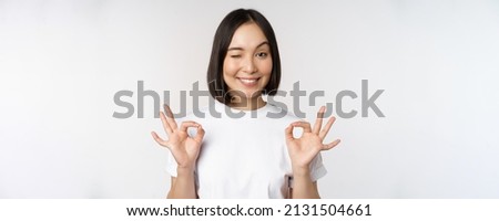 Very well, excellent. Smiling asian woman showing okay sign, approval, ok gesture, looking satisfied, recommending smth, standing over white background
