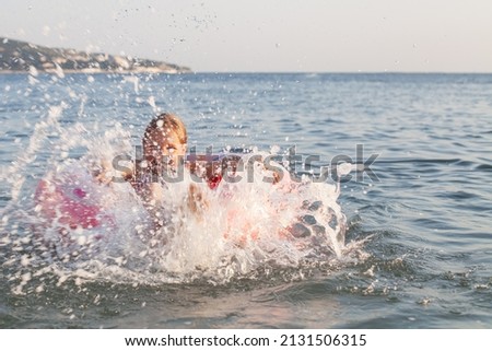 Happy girl child raises her legs and hands up in the water and splashes water drops