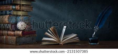 Old clock on background of old books an open book and a fountain pen in an inkwell. Сlock as a symbol of time books are symbol of knowledge. Concept on the theme of history, nostalgia, culture.  Royalty-Free Stock Photo #2131507385