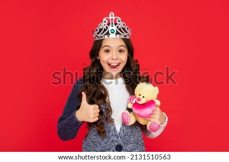 amazed child in queen crown. princess in tiara. kid hold bear toy. thumb up.