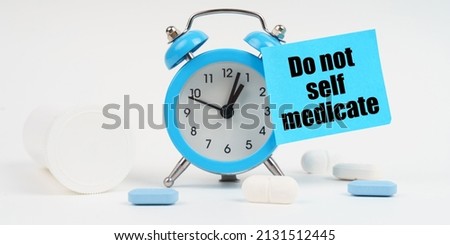 Medical concept. On a white surface there are pills and an alarm clock, on which there is a sticker with the inscription - Do not self-medicate Royalty-Free Stock Photo #2131512445