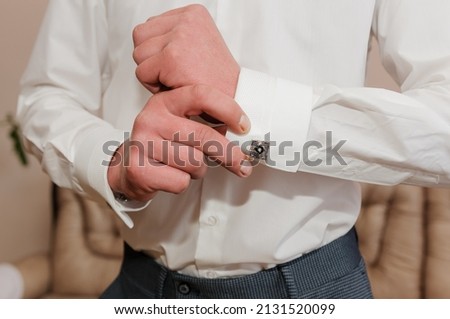 A man fastens a cufflink on his shirt