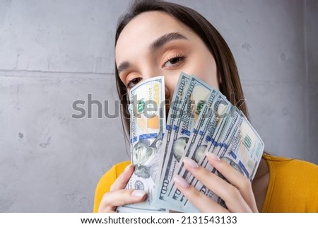 Photo of a wealthy woman in simple clothes holding a fan of dollar money isolated against a concrete wall background