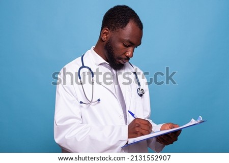 Portrait of professional doctor with stethoscope holding clipboard writing on patient chart in clinical consult. Medic in white lab coat looking at medical history and taking notes.