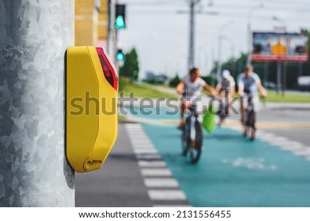 Close-up of a pedestrian crossing traffic light switch. Against the background of people and green