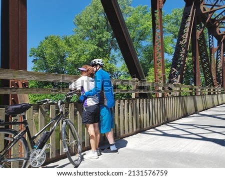 Older  bicyclists standing on old Midwestern bridge on clear summer day looking out; bicycle next the them Royalty-Free Stock Photo #2131576759