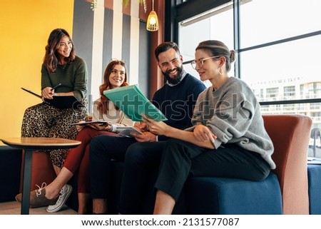Team of happy businesspeople working in an office lobby. Group of multicultural businesspeople smiling while sitting together in a co-working space. Entrepreneurs collaborating on a new project. Royalty-Free Stock Photo #2131577087