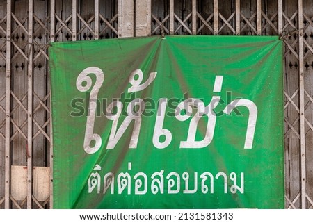 Dusty green advertising poster with Thai languages mean for rental and contact attached in front of steel door of old building inside Bangkok.