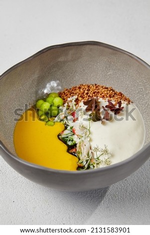 Pumpkin soup with crab in handmade ceramic bowl. Innovative recipes - cream soup with crab and cheese espuma on white concrete background. Modern food in dishware
