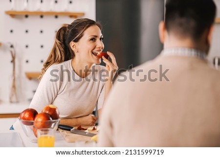 A wife eating slice of apple in kitchen and looking at husband. Royalty-Free Stock Photo #2131599719