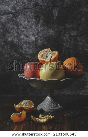 still life fruits of pear, orange and apple on on a rustic fruit tray and black background. Vertical photography. darkmood.