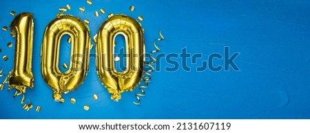 golden yellow foil balloon on blue concrete background number one hundred. Birthday or anniversary card with 100 inscription. Anniversary celebration. Banner. Royalty-Free Stock Photo #2131607119